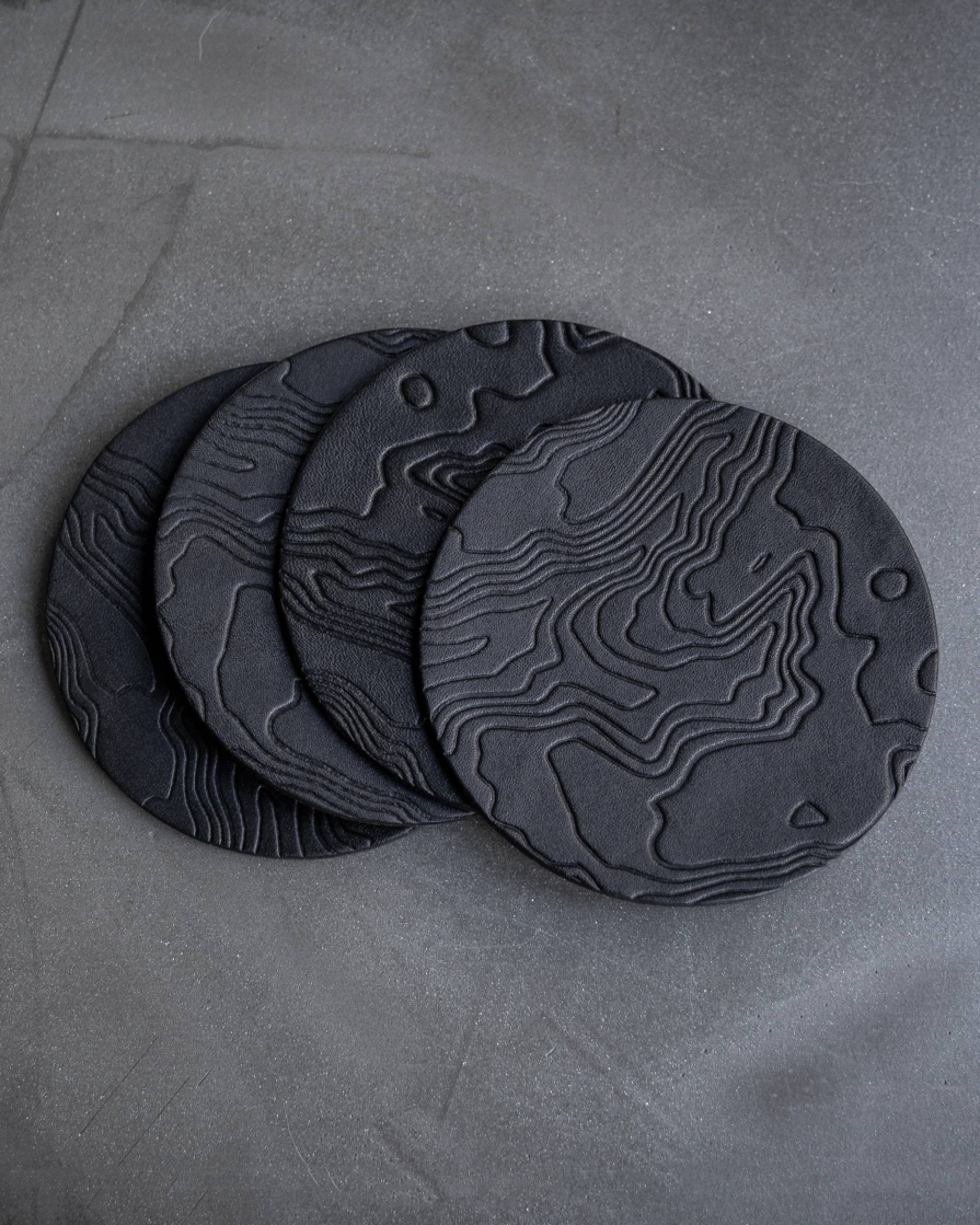 Black leather coasters featuring a topographic pattern debossed on the surface.