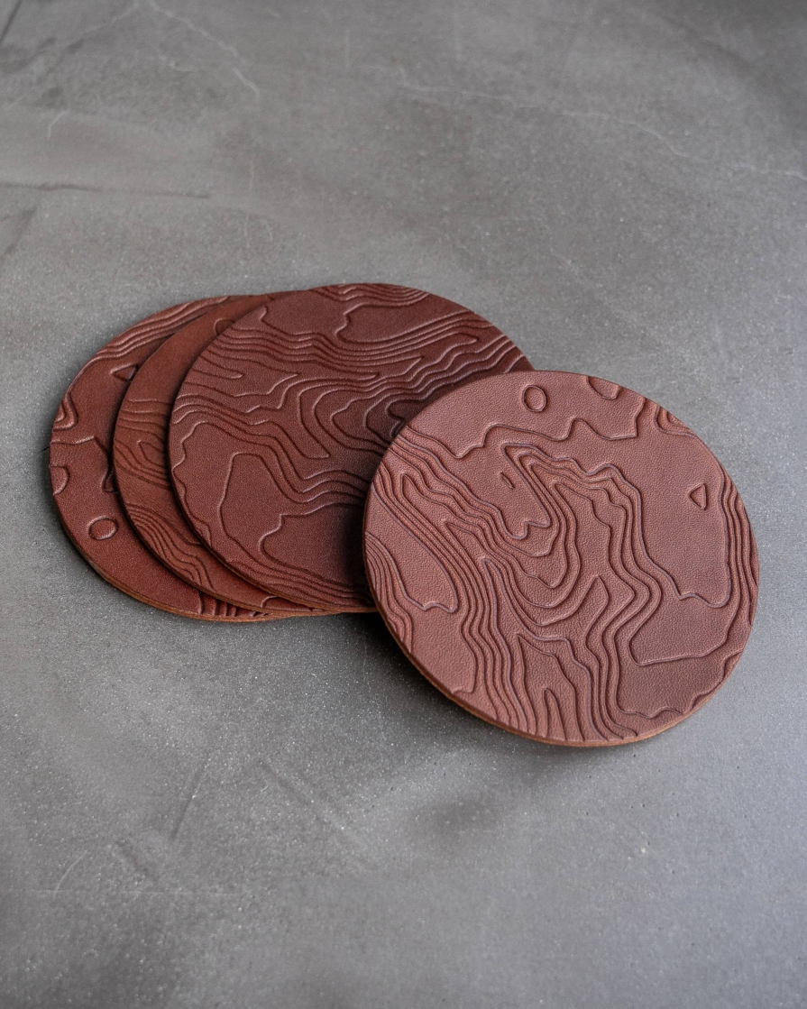 Brown leather coasters featuring a topographic pattern debossed on the surface.