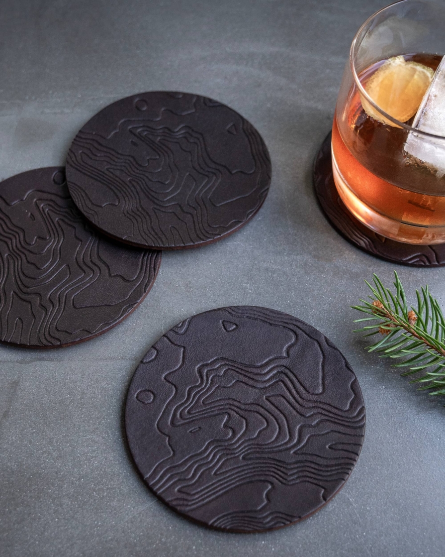 Brown leather coasters featuring a topographic pattern debossed on the surface.