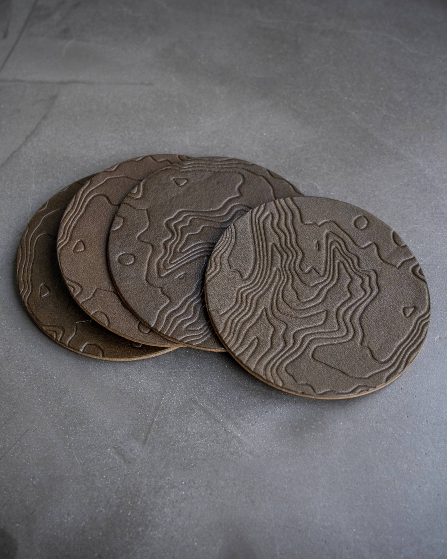 Olive leather coasters featuring a topographic pattern debossed on the surface.