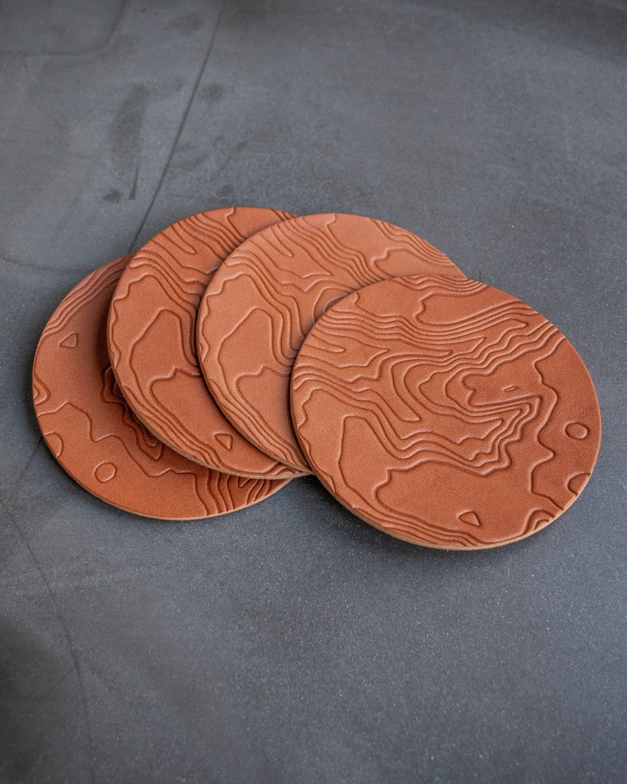 Tan leather coasters featuring a topographic pattern debossed on the surface.