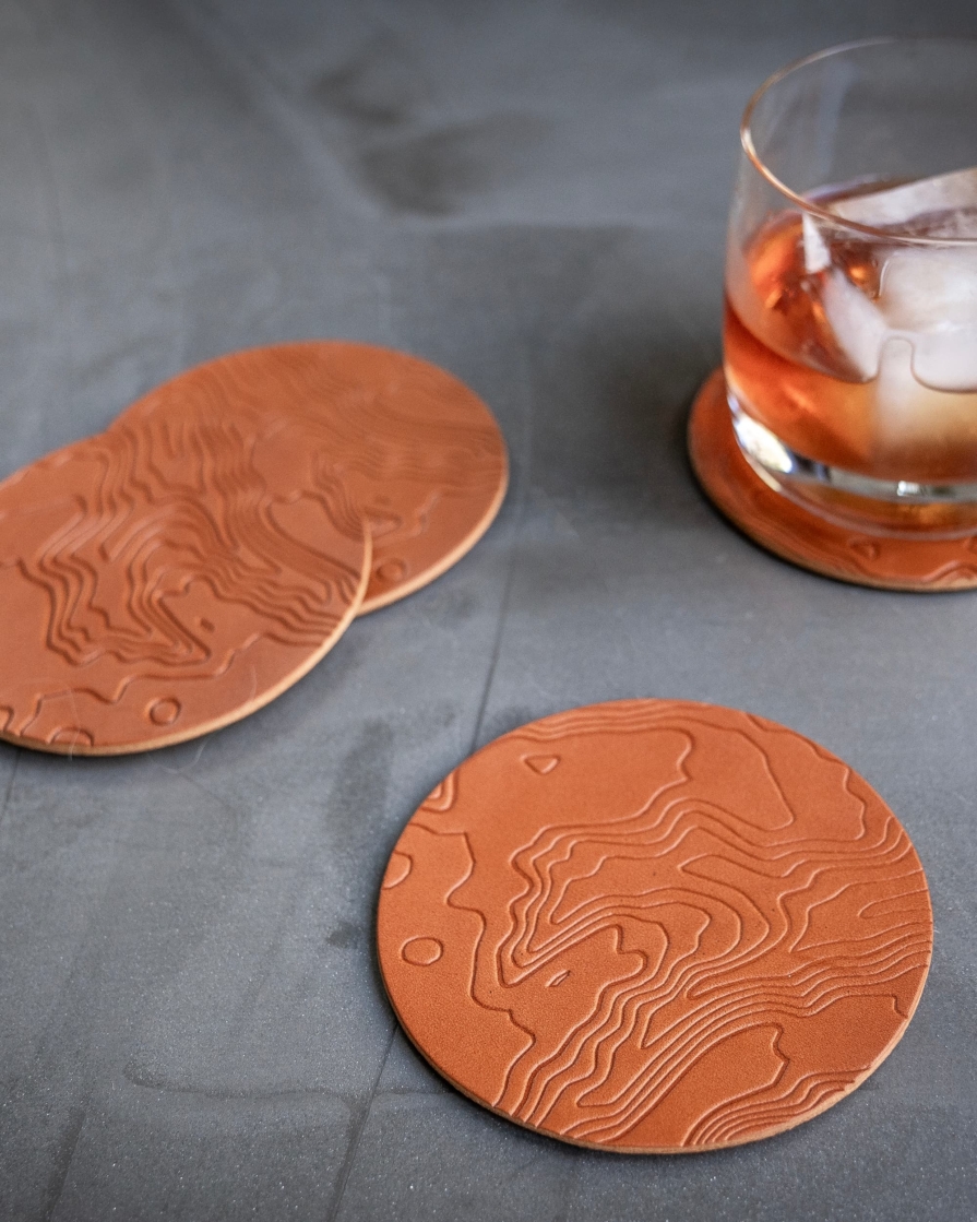 Tan leather coasters featuring a topographic pattern debossed on the surface.